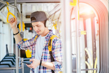 Everyday Life And Commuting To Work Or Study By Bus Tram Concept. Handsome Student Man With Headphones Is Paying Transport Ticket With Mobile Phone.