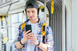 © Iryna - Everyday life and commuting to work or study by bus tram concept. Handsome student man with headphones is paying transport ticket with mobile phone.