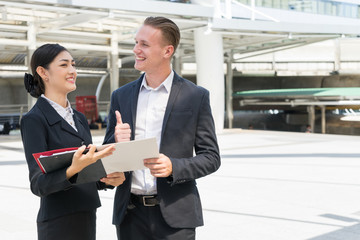 Wall Mural - Asian businesswoman talk about business future with Caucasian businessman in the city, businessman smile and show thumb up for business success idea