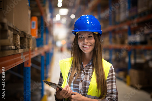 Cuadros en Lienzo Portrait of smiling woman in protective uniform with hardhat holding tablet in warehouse center