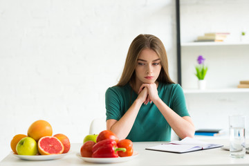 Wall Mural - sad woman sitting at table with fresh fruits and vegetables