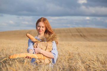 Redhead woman with bakery products in ripe wheat field.