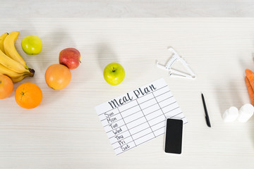 Wall Mural - top view of meal plan, smartphone with blank screen, caliper, pills and fresh fruits on wooden surface