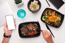 Man eating healthy food in to go boxes and holding cellphone