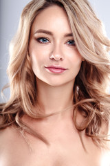 Wall Mural - Blonde young woman with healthy curly hair and natural make up . Beautiful model girl with wavy hairstyle. Care and beauty