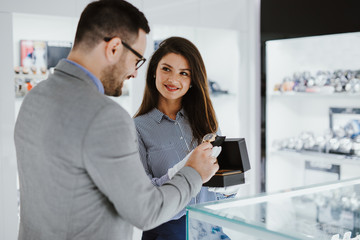 Beautiful middle age woman working in jewelry store  and showing expensive watch to male buyer.