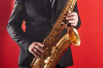 Portrait of professional musician saxophonist man in  suit plays jazz music on saxophone, red background in a photo studio