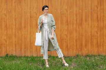 Wall Mural - Woman with short hair holding reusable coffee cup and eco bag enjoying morning. Eco friendly concept.