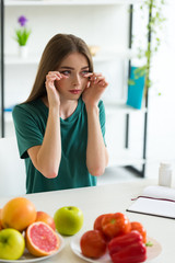 Wall Mural - girl with allergy wiping tears while sitting at table with fruits, vegetables and pills