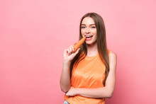 Smiling Attractive Young Woman Eating Carrot And Looking At Camera On Pink