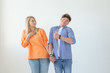 © satura_ - Young funny couple charming serious girl and a crazy young guy in casual clothes holding hands and posing on a white background. Misunderstandings in the relationship concept. Copyspace.