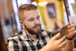 © satura_ - Stylish young man with a mustache and beard is watching a social network using a smartphone while sitting in a cafe on a weekend. The concept of dependence on social networks.