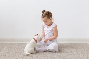 Childhood, pets and dogs concept - Little puppy and child girl in white shirt having fun