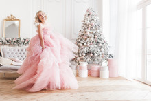 Young Beautiful Blond Woman On Christmas Background Full Height. Attractive Lady In Pink Gorgeous Dress.