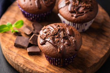 Double chocolate muffins covered with melted chocolate on a wooden background