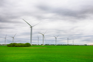 Wind power plant turbines on a green field under sky with clouds. Green energy, renewable sources, save planet