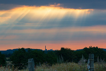 the first rays of the sun break through the dark clouds across the field