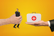 © gearstd - Man's hand exchanging tiny businessman for medical bag held in another man's hand on amber background.