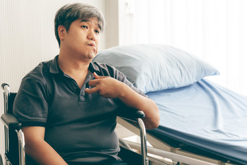 Wall Mural - Asian middle aged man  sitting on a wheelchair close to the patien bed, His hands are kinking due to a nervous system illness and paralysis, to health care concept.