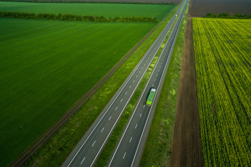 Wall Mural - green truck driving on asphalt road along the green fields. seen from the air. Aerial view landscape. drone photography.  cargo delivery
