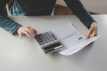 young woman using calculator for analysis and calculating family budget cost bills report on desk in home office, plan money cost saving, investment, business finance, expenses and income concept