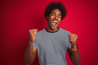 © Krakenimages.com - Young american man with afro hair wearing navy striped t-shirt over isolated red background very happy and excited doing winner gesture with arms raised, smiling and screaming for success.