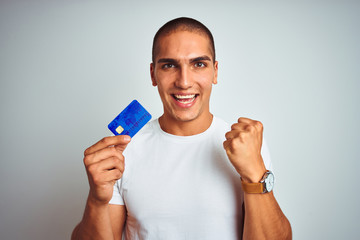 Young handsome man holding credit card over white isolated background screaming proud and celebrating victory and success very excited, cheering emotion