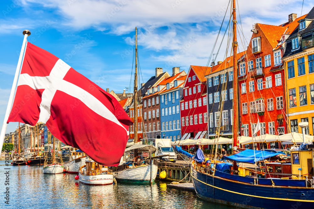 Copenhagen iconic view. Famous old Nyhavn port in the center of Copenhagen, Denmark during summer sunny day with Denmark flag on the foreground. - obrazy, fototapety, plakaty 