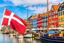 Copenhagen Iconic View. Famous Old Nyhavn Port In The Center Of Copenhagen, Denmark During Summer Sunny Day With Denmark Flag On The Foreground.