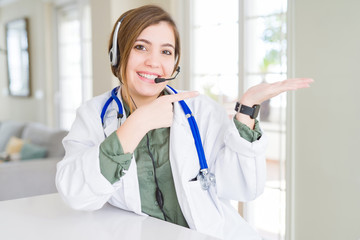 Sticker - Beautiful young doctor woman wearing headset amazed and smiling to the camera while presenting with hand and pointing with finger.