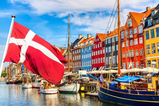 Wall Mural -  - Copenhagen iconic view. Famous old Nyhavn port in the center of Copenhagen, Denmark during summer sunny day with Denmark flag on the foreground.