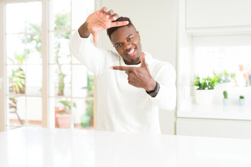 Poster - Handsome african american man on white table smiling making frame with hands and fingers with happy face. Creativity and photography concept.