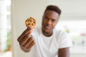 Poster - Young african american man eating chocolate chips cookies with a confident expression on smart face thinking serious