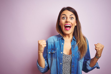 Wall Mural - Young beautiful woman standing over pink isolated background celebrating surprised and amazed for success with arms raised and open eyes. Winner concept.