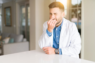 Sticker - Young handsome doctor man at the clinic smelling something stinky and disgusting, intolerable smell, holding breath with fingers on nose. Bad smells concept.