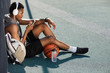© Seventyfour - High angle portrait of contemporary African-American man wearing headphones and using smartphone while sitting in basketball court outdoors, copy space