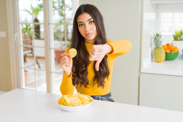 Sticker - Young woman eating fastfood potato chips with angry face, negative sign showing dislike with thumbs down, rejection concept