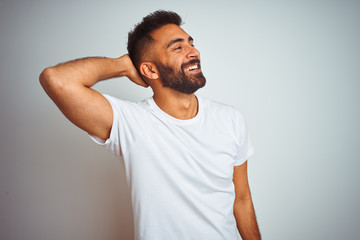 Young indian man wearing t-shirt standing over isolated white background smiling confident touching hair with hand up gesture, posing attractive and fashionable