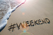© lazyllama - Modern travel message for the beach with a social media-friendly hashtag written with the word 'weekend' in smooth sand with incoming wave