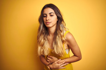 Canvas Print - Young beautiful woman wearing t-shirt over yellow isolated background with hand on stomach because indigestion, painful illness feeling unwell. Ache concept.