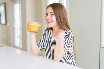 Wall Mural - Beautiful young girl kid drinking a glass of fresh orange juice with surprise face pointing finger to himself