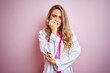 © Krakenimages.com - Young beautiful doctor woman standing over pink isolated background looking stressed and nervous with hands on mouth biting nails. Anxiety problem.