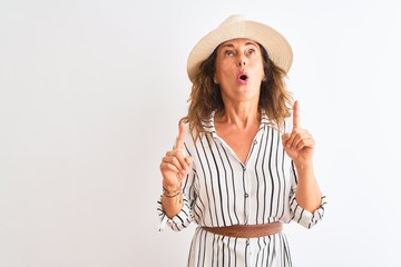 middle age businesswoman wearing striped dress and hat over isolated white background amazed and sur