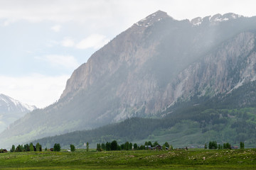 Mount Crested Butte village in summer with sun rays or rain and mountain cliff with alpine meadows in early summer