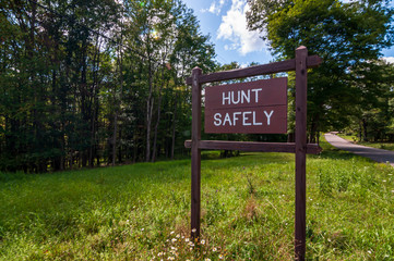 A wooden sign saying HUNT SAFELY on the side of a road in Warren county, Pennsylvania, USA on a sunny, summer day