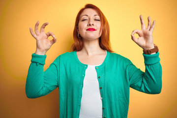 Sticker - Youg beautiful redhead woman wearing winter green sweater over isolated yellow background relax and smiling with eyes closed doing meditation gesture with fingers. Yoga concept.