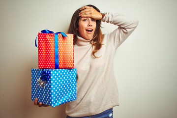 Wall Mural - Young beautiful woman holding birthday gifts standing over isolated white background stressed with hand on head, shocked with shame and surprise face, angry and frustrated. Fear and upset for mistake.