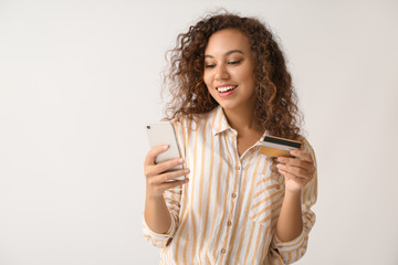 Canvas Print - Beautiful African-American woman with credit card and mobile phone on light background