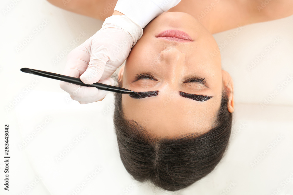 Young woman undergoing eyebrow correction procedure in beauty salon