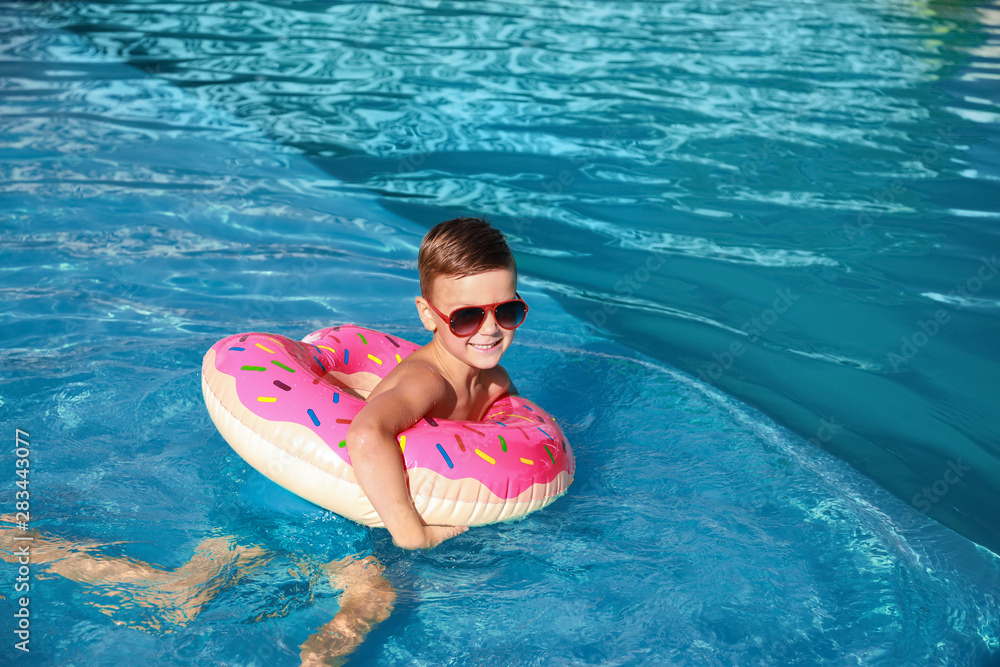 Cute little boy with inflatable ring swimming in pool